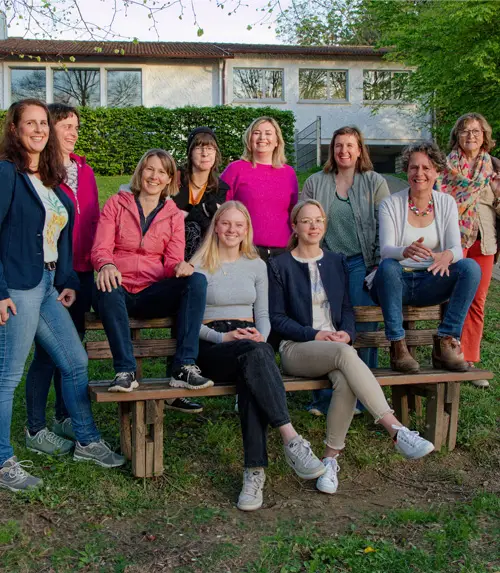 Die Frauen der Frauenliste Heuweiler sitzen und stehen gemeinsam um eine Holzbank auf einer Wiese.
